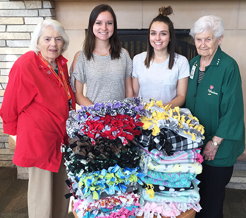 2 elderly ladies and 2 high school girls standing with a pile of handmade blankets